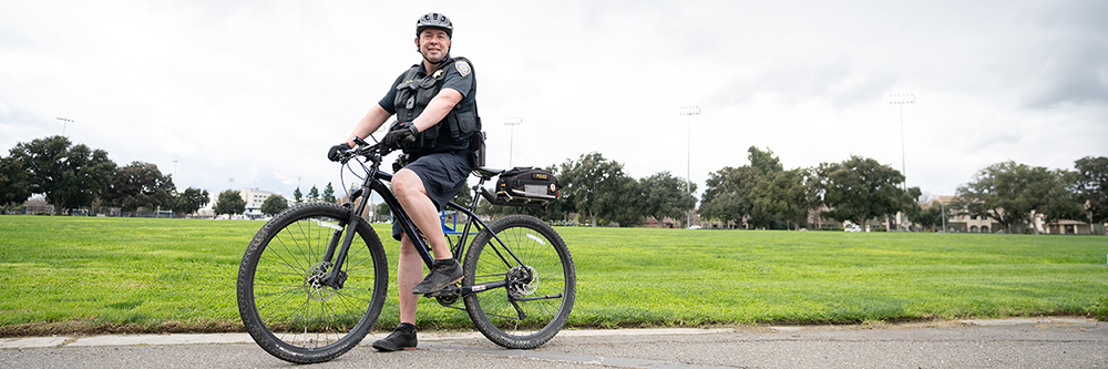 UC Davis Police officer on a bike at Hutchison field looking out across campus.