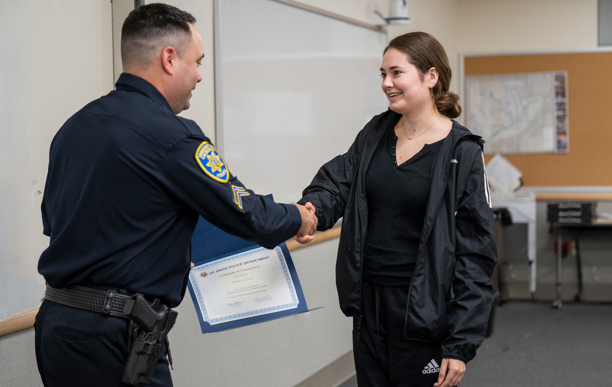 young woman shakes the hand of a police officer, who is handing her a diploma