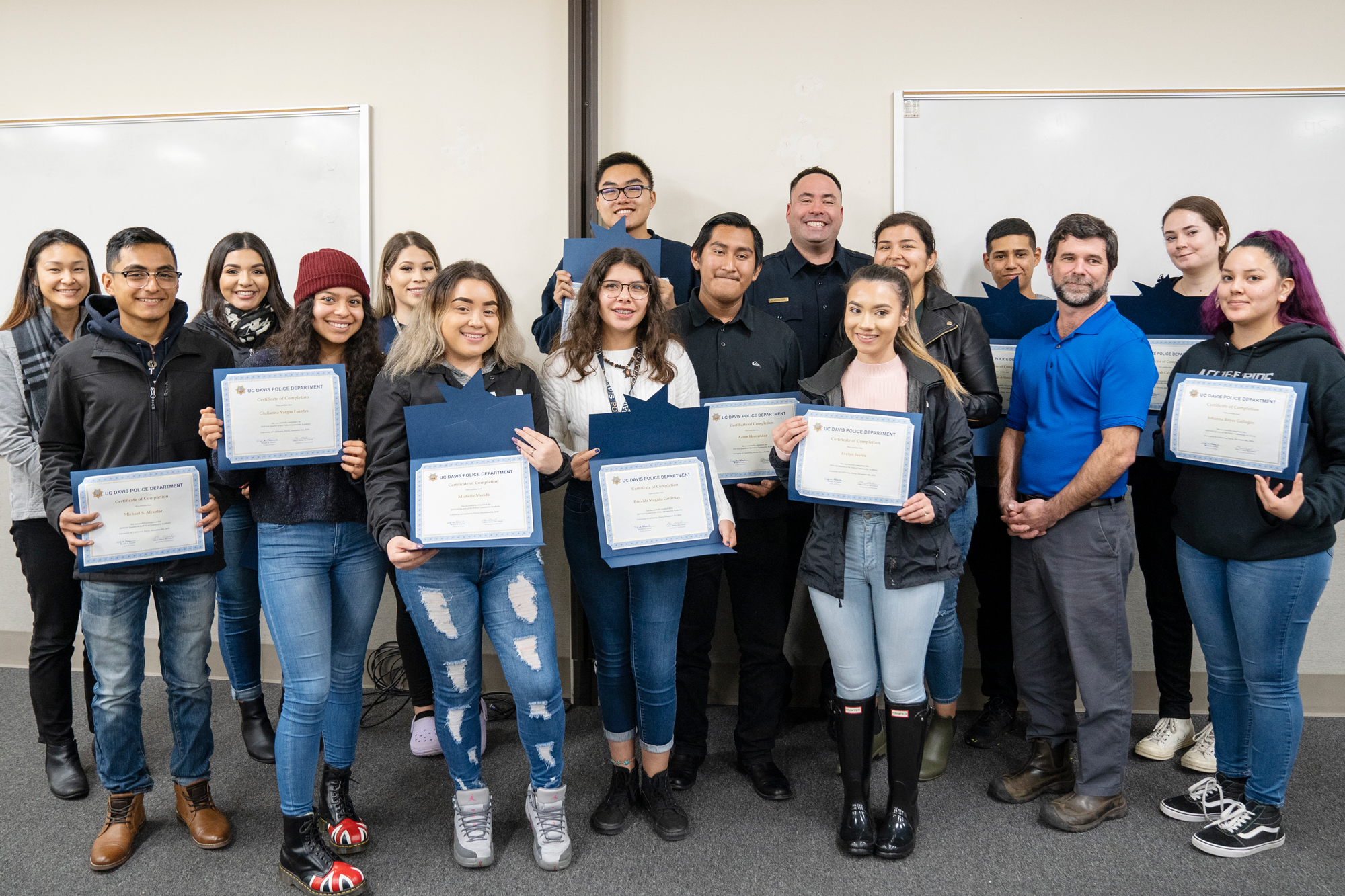 Group photo of students smiling with certificates and beaming police officer in the back row