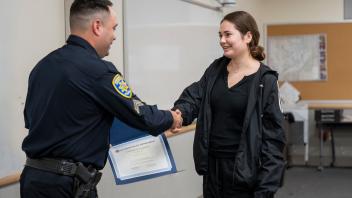 young woman in tracksuit shakes the hand of police officer, as he hands her certificate