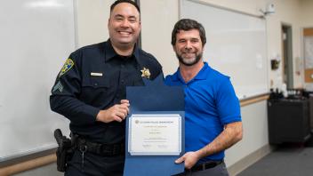 UC Davis police officer with staff member and certificate, smiling