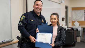 UC Davis police officer with student and certificate, smiling