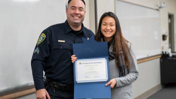 UC Davis staff member with campus police officer and certificate, smiling