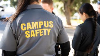 Back view of campus safety specialist in gray shirt with yellow 'CAMPUS SAFETY' text.