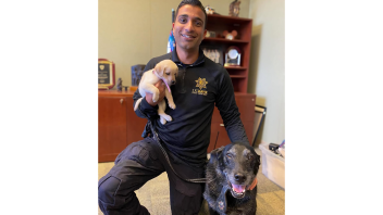 K9 Charlie sitting next to CORE officer Malik who is holding up puppy K9 Cali.