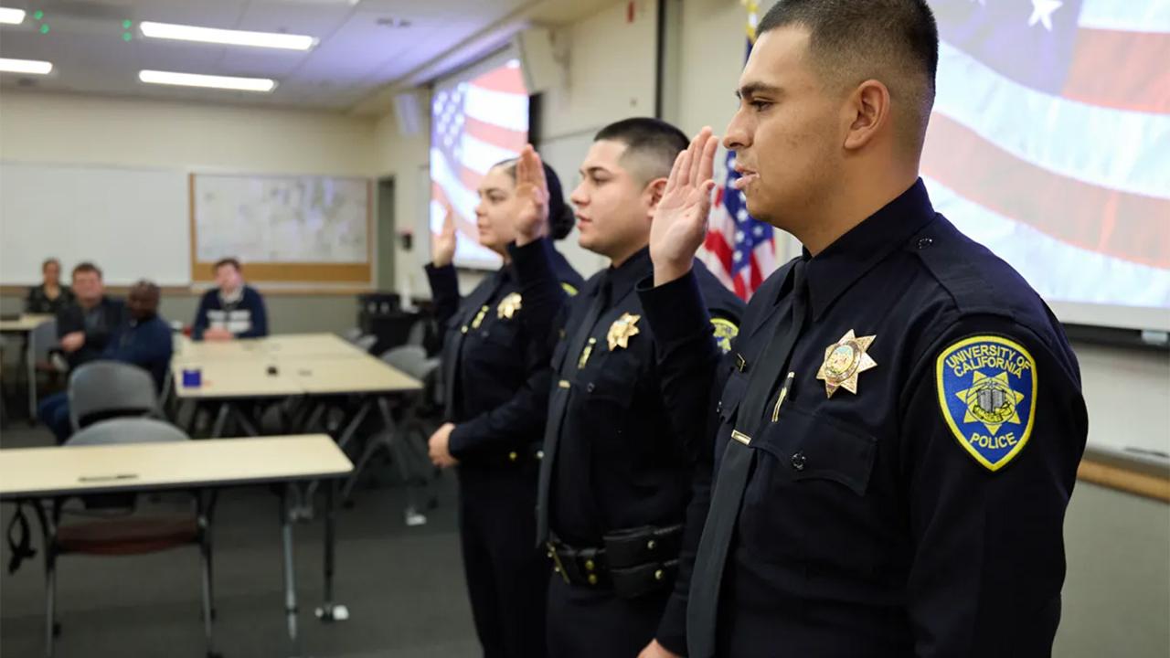 At right, UC Davis police officer Ernesto Moron repeats an oath along with fellow officers David Barilles and Daniella Flores at their swearing-in ceremony at the UC Davis Police department on Dec. 22, 2023. Photo by Fred Greaves for CalMatters.