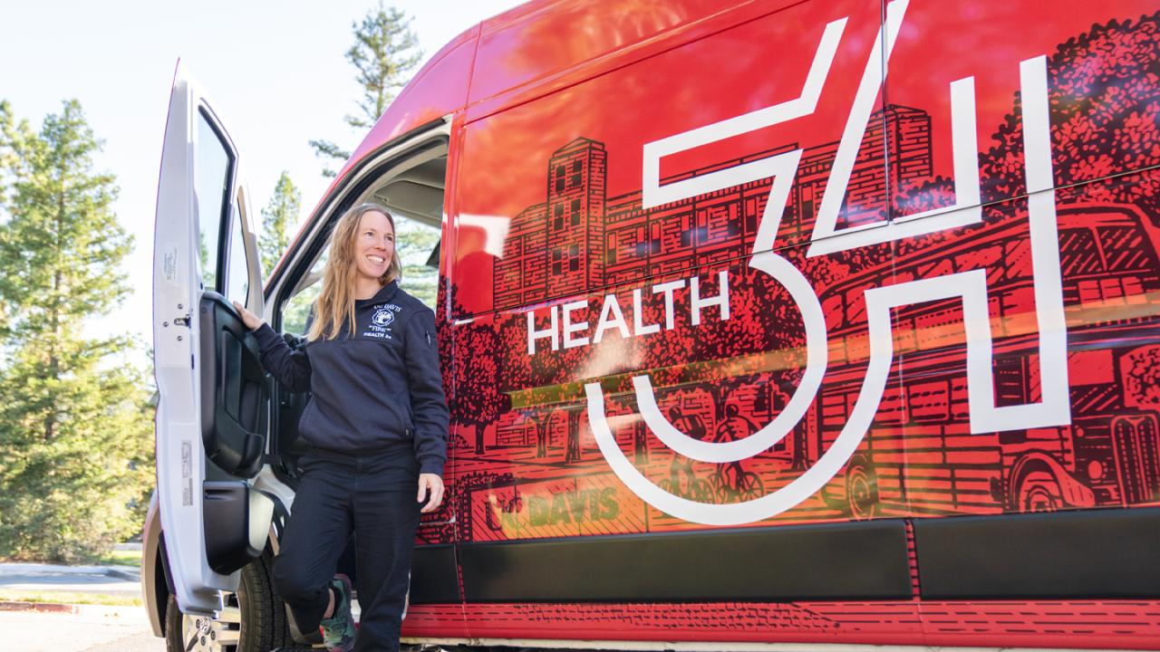 Health 34 staff smiling and stepping out of bright red van branded with the Health 34 logo.