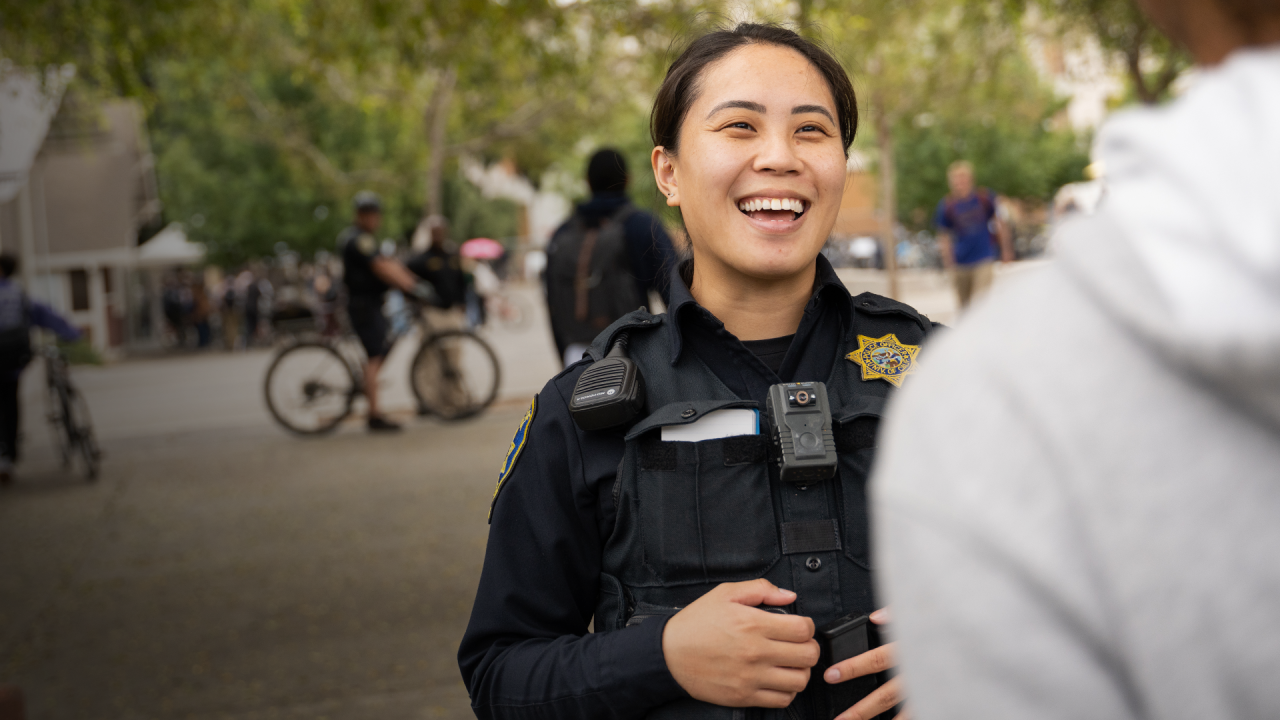 UC Davis Police Officer smiling and talking to a student outside of the Silo on Campus.
