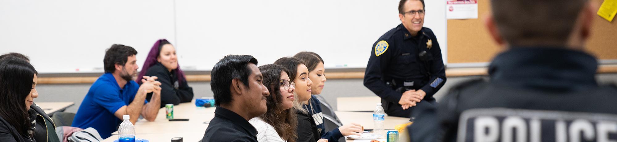 Police captain smiling with students listening in a classroom