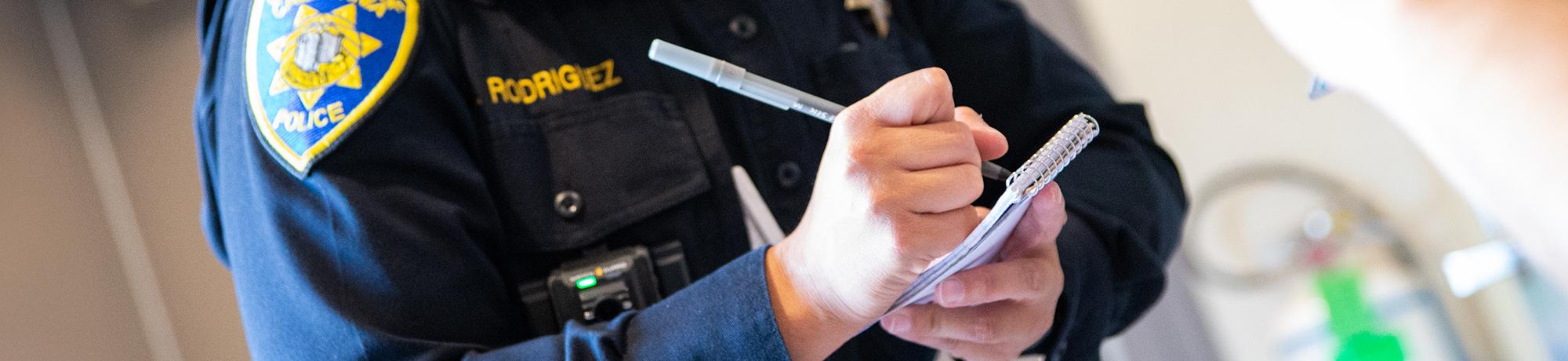 Close-up of hands of a UC Davis Police Officer writing something down on their notepad.